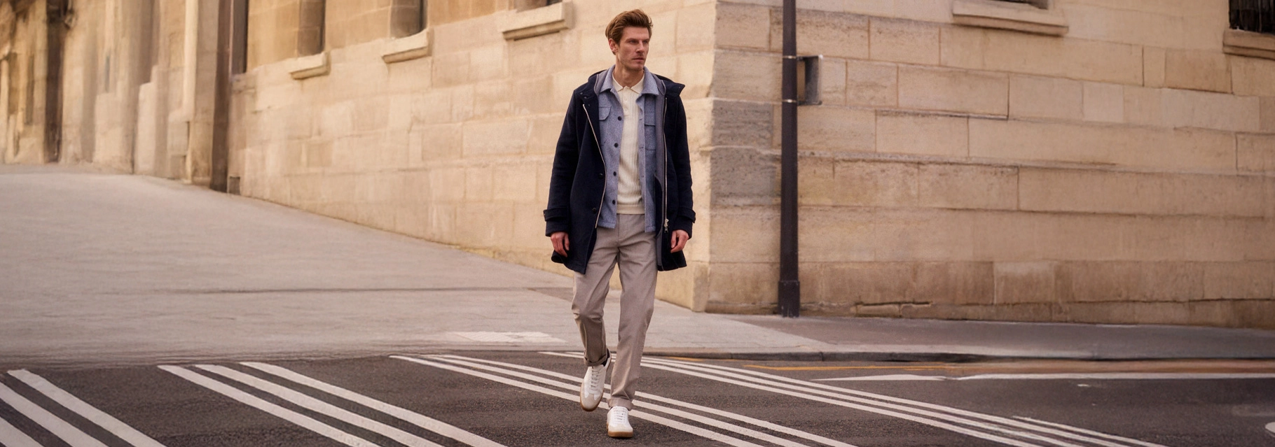 Man draagt een lichte Pierre Cardin herenbroek met donkerblauwe jas en witte sneakers